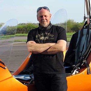 Nikolaus Jost mit verschränkten Armen vor dem orangen Tragschrauber